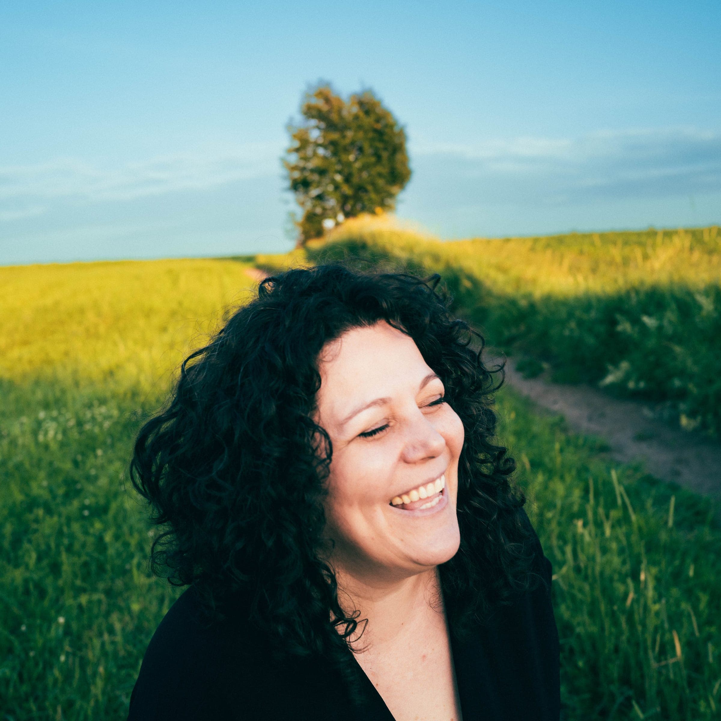 Karine Champagne éclate de rire, les yeux fermés, dans un champ au soleil couchant.