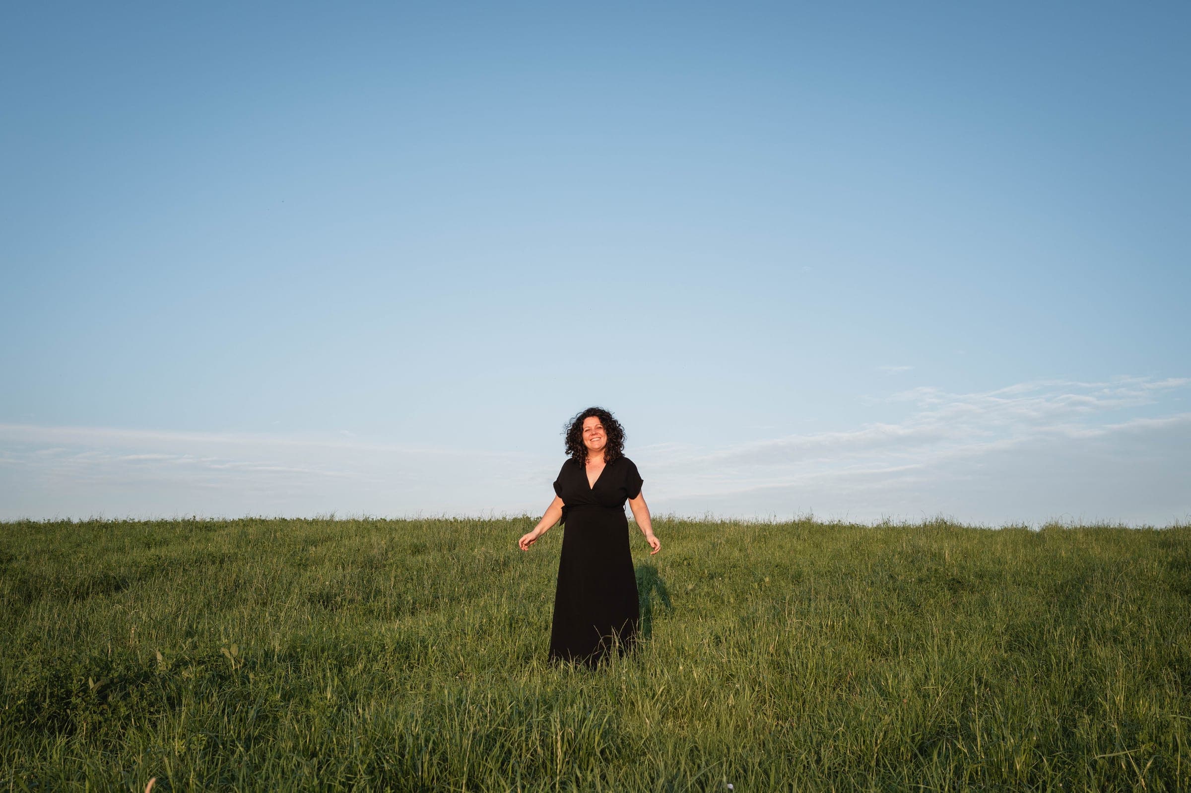 Karine, toute petite en robe noire, au milieu d'un grand pré sous un immense ciel bleu.